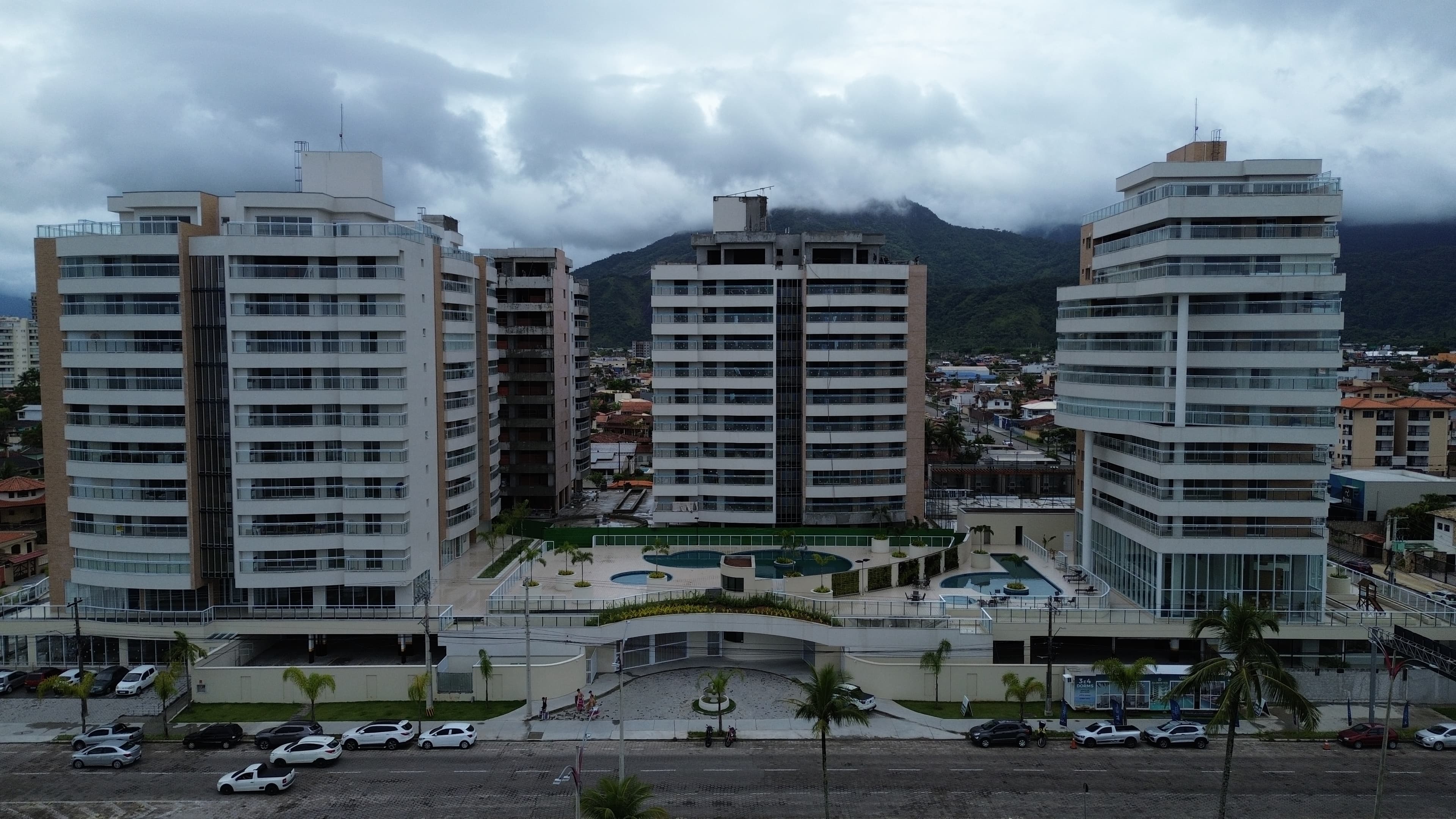 Condomínio de torres residenciais no litoral com área de lazer e piscinas, serra ao fundo